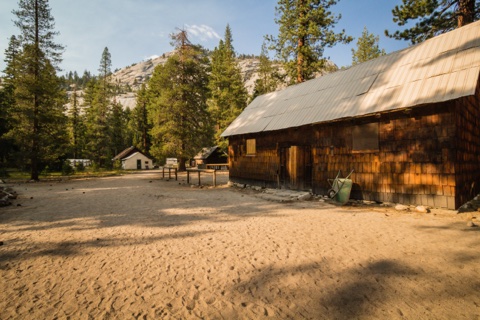 The main clearing at golden hour, with the shingle-sided main building at right and granite domes rising behind the trees.