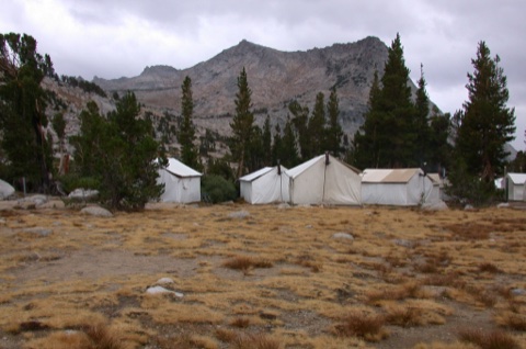 Guest tent cabins on the alpine meadow bench, rocky ridgeline behind, under a gray Sierra sky.