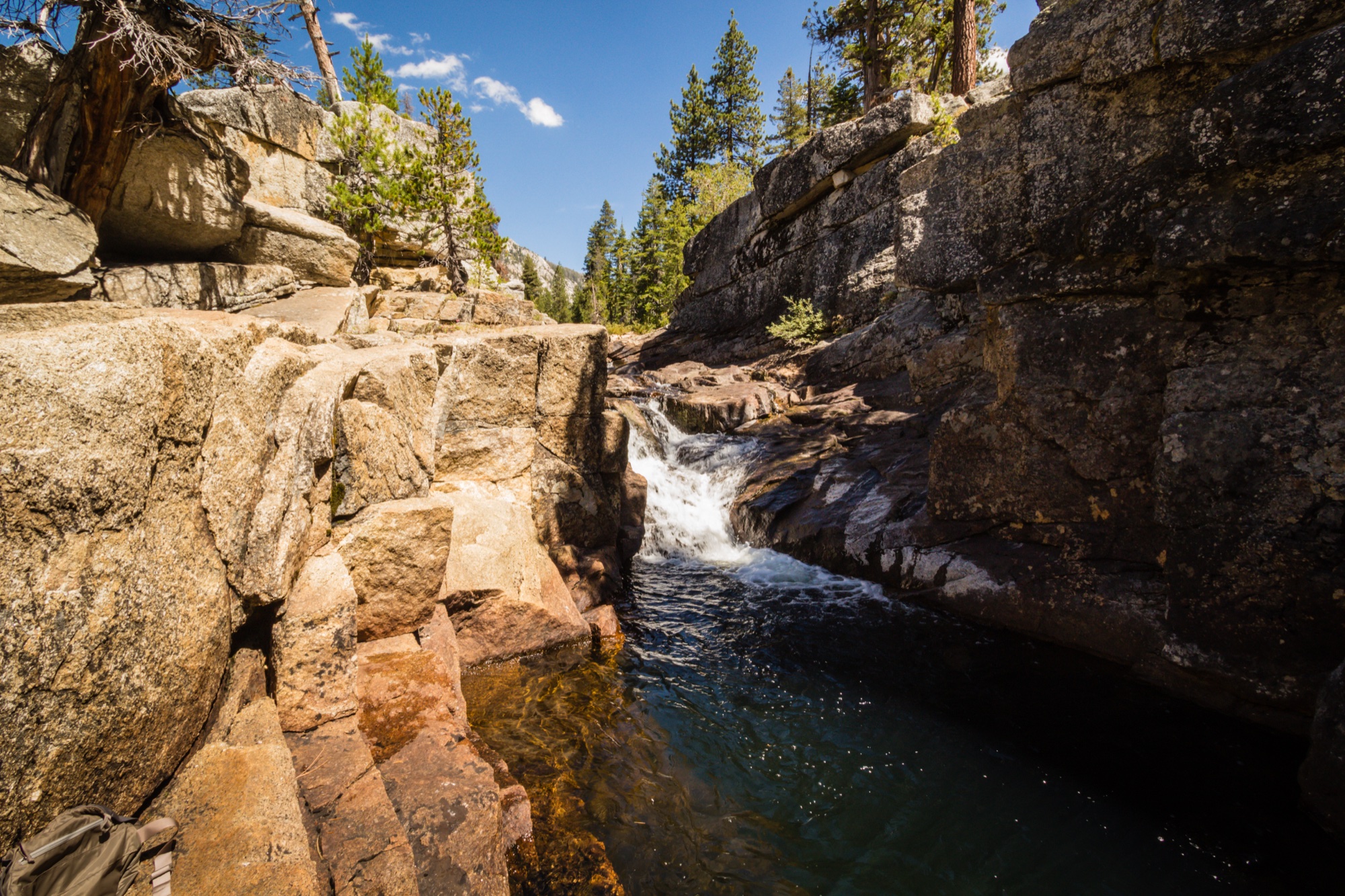 A cascade pouring into a clear pool in a granite gorge